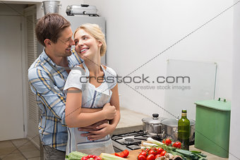 Happy couple embracing while preparing food in kitchen