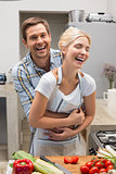 Cheerful couple embracing while preparing food in kitchen