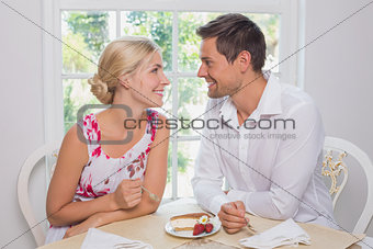 Loving couple with pastry looking at each other at dining table