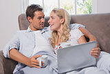 Relaxed loving couple with coffee cups using laptop on sofa