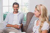 Relaxed couple with coffee cups sitting in living room