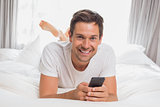 Happy casual young man text messaging in bed