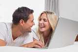 Cheerful relaxed casual couple using laptop in bed