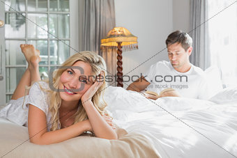 Relaxed woman with man reading book in background on bed