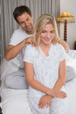 Smiling man massaging woman's shoulders in bed