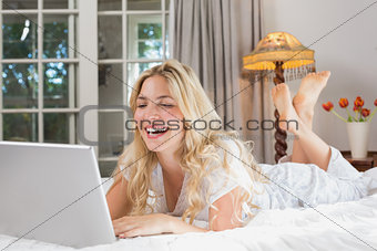 Cheerful casual woman using laptop in bed