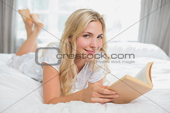 Beautiful young woman reading book in bed