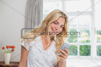 Young woman reading text message in bed