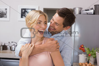 Cheerful man embracing woman from behind in kitchen