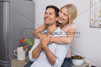 Cheerful woman embracing man from behind at home