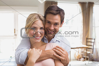 Happy man embracing woman from behind at home