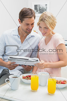 Couple reading newspaper while having breakfast at home
