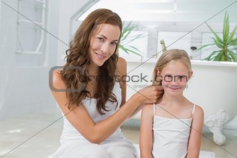 Smiling woman braiding cute little girl's hair in bathroom