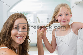 Portrait of a smiling woman braiding cute little girl's hair