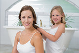 Cute little girl braiding mother's hair in bathroom