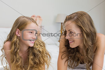 Smiling mother and daughter lying in bed