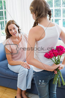 Girl surprising mother with flowers in bedroom