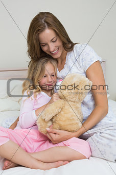 Woman and girl playing with stuffed toy in bedroom