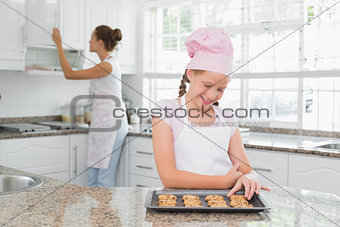 Girl looking at freshly prepared cookies with mother in kitchen