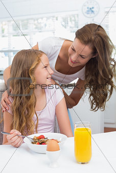 Mother looking at daughter while having breakfast in kitchen