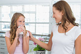 Girl drinking milk as she looks to her mother in kitchen