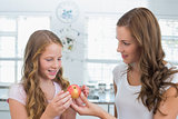 Mother giving apple to her daughter in kitchen
