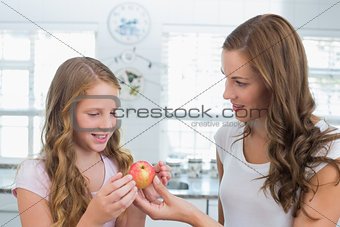 Mother giving apple to her daughter in kitchen