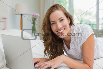Beautiful smiling woman using laptop in bed