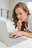 Beautiful serious woman using laptop in bed