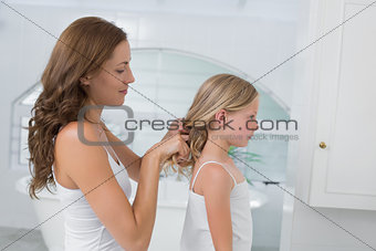 Woman braiding cute little girl's hair in bathroom