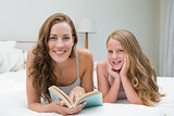 Girl and mother with book lying in bed