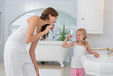Girl brushing teeth as she looks at her mother