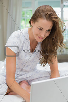 Smiling woman using laptop in bed