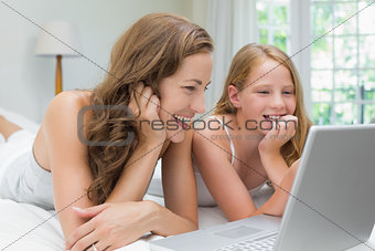 Happy mother and daughter using laptop in bed