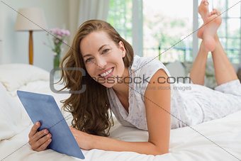 Happy young woman using digital tablet in bed