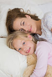 Girl and mother with stuffed toy resting in bed
