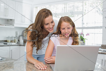 Happy mother and daughter using laptop in kitchen