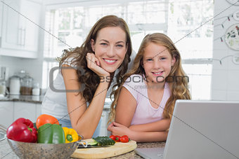 Happy mother and daughter using laptop in kitchen