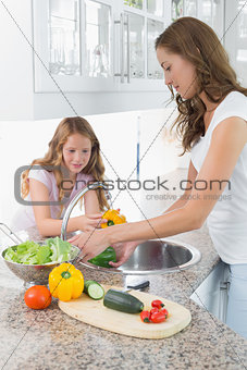 Girl helping her mother to wash vegetables in kitchen