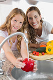 Portrait of young girl helping her mother to wash vegetables