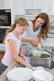 Girl helping her mother to wash utensils in kitchen