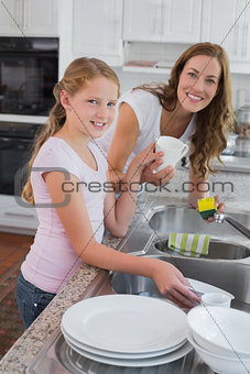 Girl helping her mother to wash utensils in kitchen