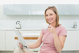 Relaxed woman with newspaper having coffee in kitchen