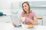 Concentrated woman reading newspaper while having coffee in kitchen