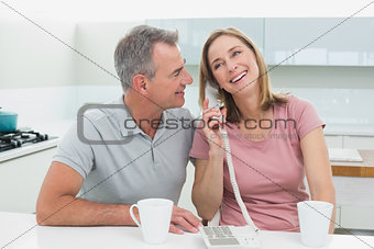 Happy couple using landline phone in kitchen