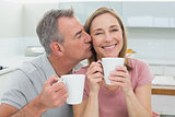 Man kissing a happy woman while having coffee in kitchen