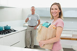 Woman carrying grocery bag while man with coffee cup in kitchen