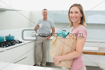 Woman carrying grocery bag while man with coffee cup in kitchen