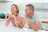 Happy relaxed couple with coffee cups in kitchen