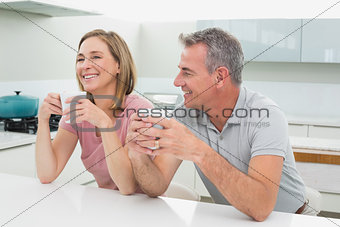 Happy relaxed couple with coffee cups in kitchen